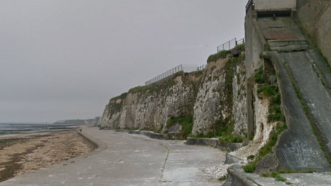 A Google Street image of a stretch of concrete promenade with a short, white chalk cliff behind it to the right, and the beach to the left.