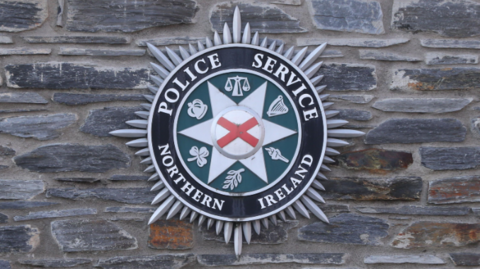 Shows the logo of the Police Service of Northern Ireland on a wall