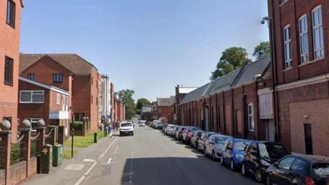 Raglan Street with a line of cars parked down one side of the road. There is a mixture of homes and business premises.