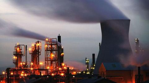 Grangemouth at dusk with chimneys and industrial towers lit by orange lights