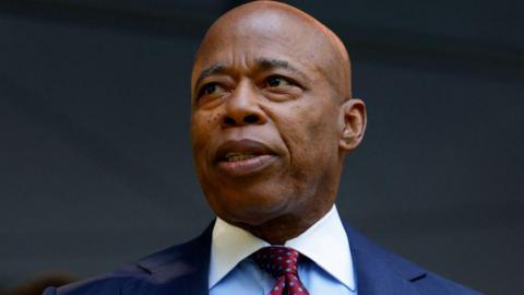 A file photo of Eric Adams, who is looking off to the left and wearing a blue suit coat, a white shirt and a red tie. 