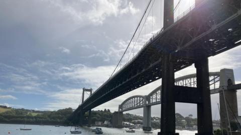 Two bridges are in this shot over the River Tamar.  The A38 road bridge is to the left of the Royal Albert Bridge designed for the railways by Isambard Kingdom Brunel which opened in 1859.
Small boats are on the river below.