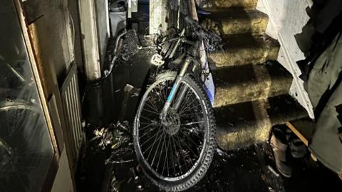 The wreckage of a house fire with a burned e-bike in the downstairs hallway.