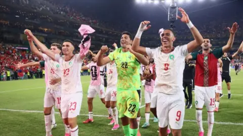 Morocco players hold their arms aloft, with broad smiles, after their victory