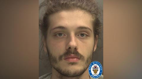 A police mugshot of a man with a beard and brown hair. He is looking directly at the camera. There is a West Midlands Police emblem in the bottom right hand corner of the image.