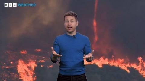 Tomasz Shafernaker stands in front of a picture of the ground on fire and a firenado