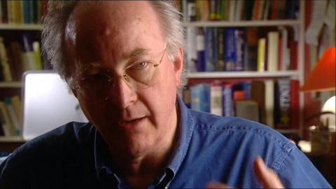 Philip Pullman sits in front of rows of books.