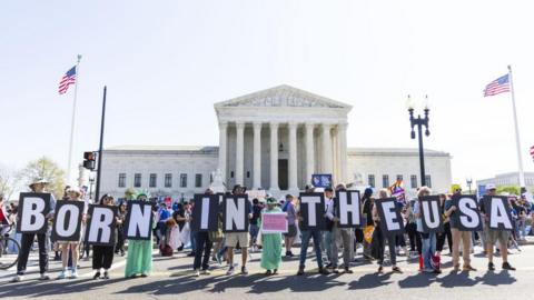 Protesters gather outside the Supreme Court holding signs that read "Born in the USA"