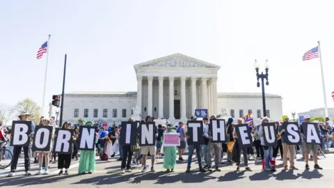 Protesters gather outside the Supreme Court holding signs that read "Born in the USA"