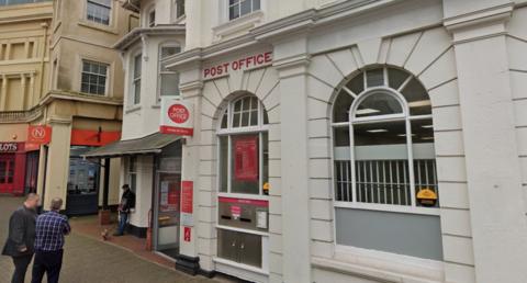 The exterior of the Post Office in Teignmouth with two men standing talking in the bottom left-hand corner of the shot