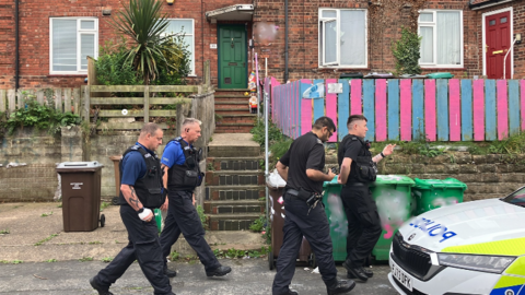 Police walking down Costock Avenue, Sherwood, on the morning of the tragedy. Four officers walk together down a residential street.