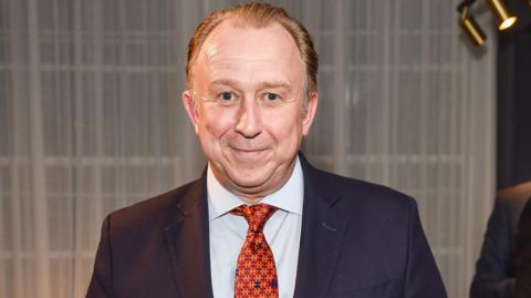 Nigel Blow wearing a blue suit and orange tie at the opening of the Turnbull and Asser store in Mayfair, 2015