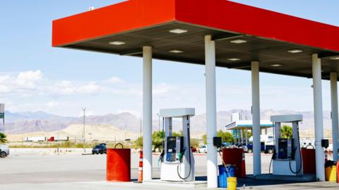 A petrol station with a bright red awning sits in the foreground, with a long mountain range in the background.