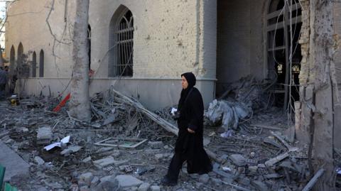 A woman walks through debris of a damaged building at the Sharif University in Tehran, Iran