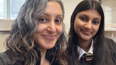 Sharan (pictured on the left) sits with her daughter Simran. Simran is 15 and is wearing her school uniform.