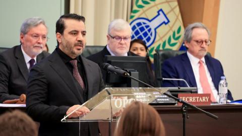 Syrian Foreign Minister Asaad al-Shibani wears a dark suit and addresses a meeting of the Executive Committee of the OPCW in The Hague on 5 March 2025. There are three men with grey hair and glasses and wearing suits seated behind him and a woman seated in the background. 