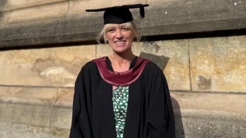 A woman wears a gradation cap and gown to collect her degree.