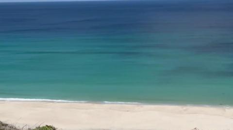 A sandy beach with blue sea beyond looked at from a cliff.