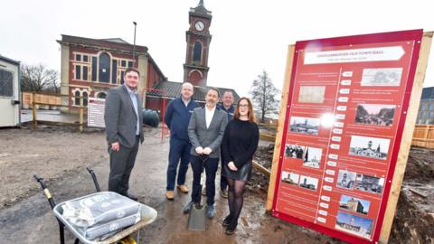 Middlesbrough Mayor Chris Cooke, contracts manager Jonathan White, managing director Paul Hammerton, project manager Mike Hamm and Middlesbrough Council's capital development manager Claire Bell are stood at the town hall building with a timeline of its history beside them.