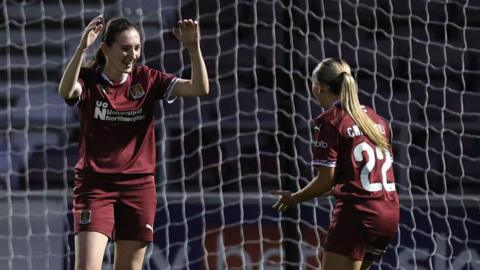 Mia Richards of Northampton Town celebrates with Laila Channell after scoring her side's second goal, both wearing claret-coloured strip and standing in front of the goal net