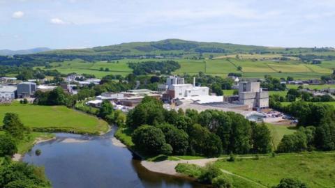 White factory in a green landscape with a pond and several trees.