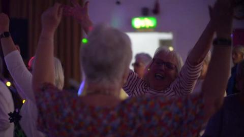 Two women dance at an event and wave their hands up in the air while smiling.