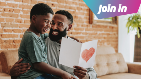 a child sitting on his dad's knee, the dad is holding a white card with a red heart drawn on it, there's a badge that reads 'join in' in the top right hand corner.
