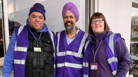 Three volunteers in purple hi-vis vests
