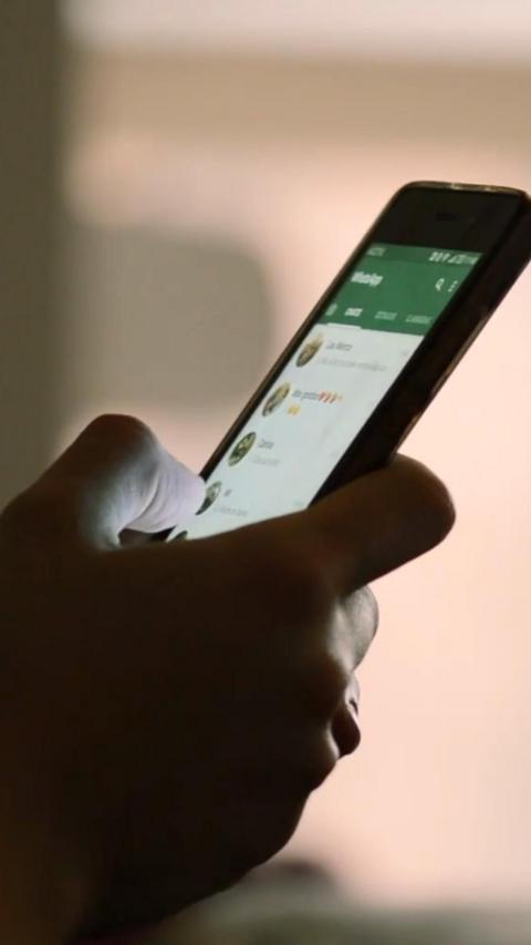 Close-up of a hand holding a smart phone. The screen of the phone is lit and the hand is in silhouette