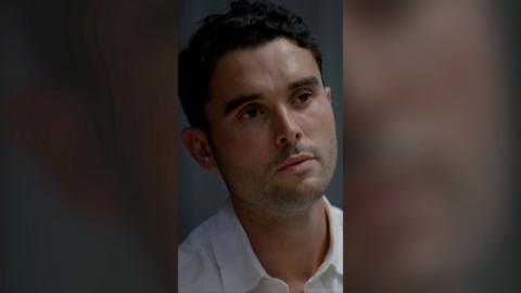 A man with dark hair looking to the side.