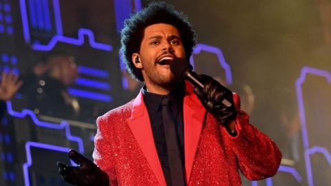 Singer The Weeknd holding a microphone and wearing a bright red jacket