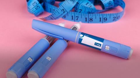 Three, blue weight-loss jabs in front of a blue tape measure sit on a pink backdrop. 