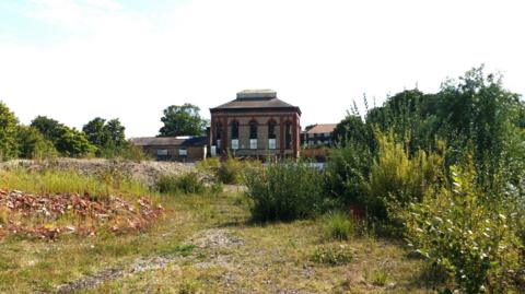 The Victorian Pump House in Eastbourne seen from a distance, with vegetation and a basic footpath in the foreground.