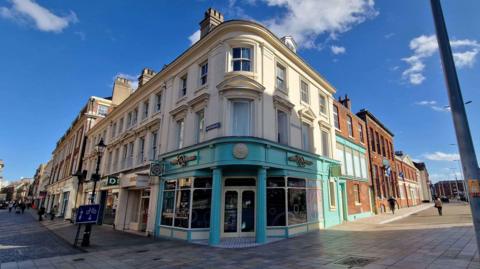 Corner building in beige with a light blue lower frontage in a Hull shopping precinct.