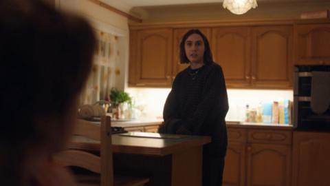 Young woman stands in a kitchen looking surprised 