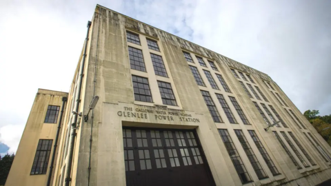 The Glenlee Power Station - a tall modernist building - with the words The Galloway Water Power Scheme above the name of the station. It is underneath a cloudy sky.