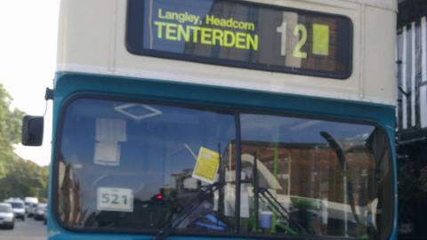 A blue and white bus at a bus stop with a parking ticket on the window