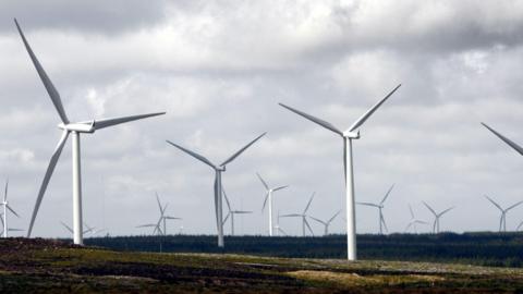 An array of wind turbines on the moorland, set against a cloudy sky.