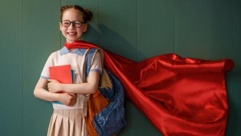 girl dressed up as a superhero holding books
