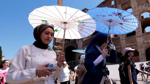 Tourists walk under parasols as they visit the Colosseum in Rome