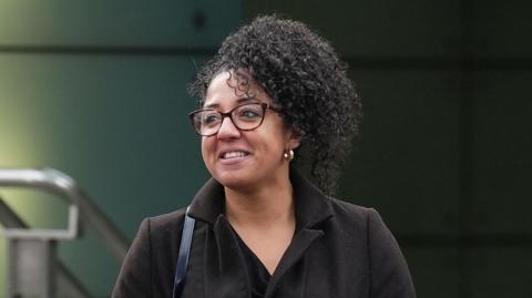 A photo of PC Korell outside the police building where the misconduct panel took place. She is wearing glasses, a dark coat and a black dress and a handbag strap is visible on her right shoulder.