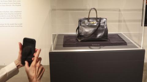 Jane Birkin's original large black leather bag sits in a glass case 