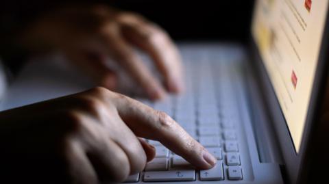 A woman is typing on a laptop keyboard. An indistinguishable page of text is on the screen.