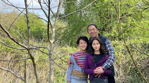 Yeshi Jampa and his children smiling whilst standing next to the walnut tree.