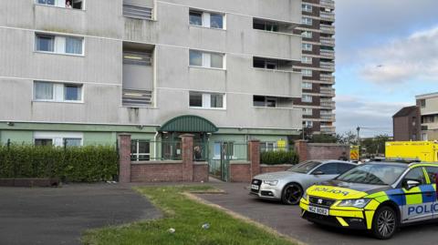 A large building. Parked in front of the building are two ambulances, as well as a police car.