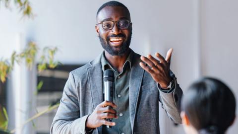 A smiling man in a suit talking into a microphone