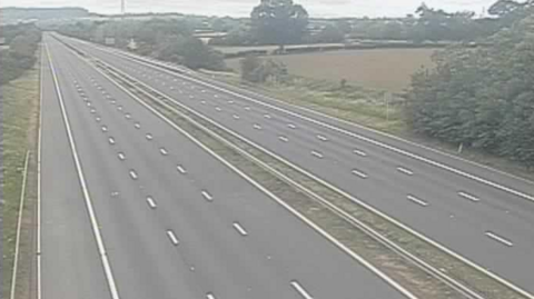 The M5 early on Saturday morning with no cars on it at all. There are fields and trees on either side of the motorway and the sky is grey. 