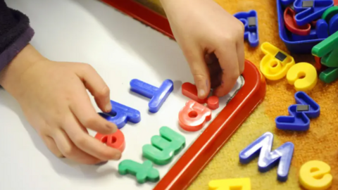 A close up of a child's hands playing with magnetic letters.