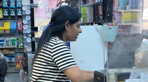 Kinnari Patel serving in the Londis in Broadstairs, where she wears a black and white striped t-shirt.