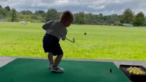 A small boy on a driving range hitting a golf ball